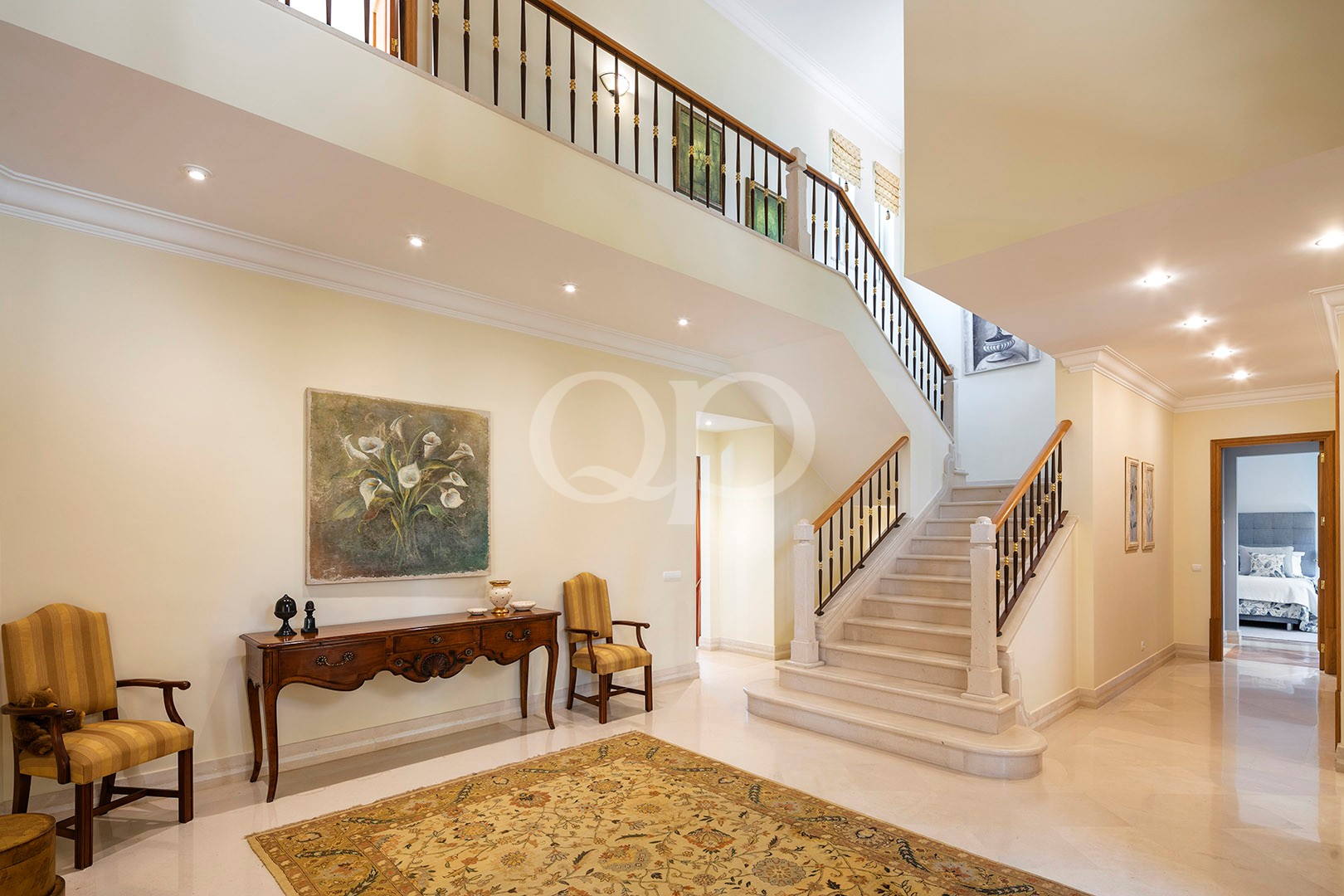 Elegant two-story foyer with a curved staircase, cream walls, and a patterned rug in a luxurious home interior.