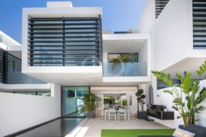 Moderne Fassade eines weißen Hauses mit Glastüren, einem Esstisch im Freien und einem rechteckigen Pool auf der Terrasse.
