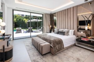 Luxuriöses Hotelzimmer mit einem Kingsize-Bett, einer bequemen Bank am Fußende und Glasschiebetüren, die zum Außenpoolbereich führen.