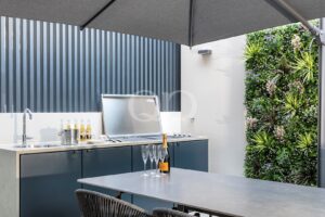 Outdoor kitchen with grill, sink, and counter, and a table set with a champagne bottle and four fluted glasses.