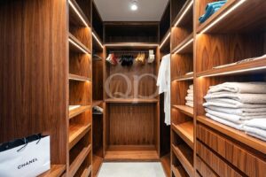 Walk-in wooden closet with built-in shelves and warm lighting, clothes hanging in the center and folded towels on right shelves.
