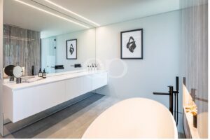 Modern bathroom with a white floating vanity, wide mirror, and black fixtures; a freestanding bathtub curves in the foreground.