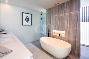 Modern spa-like bathroom with a white freestanding oval tub against a gray marble wall and illuminated recessed shelf.