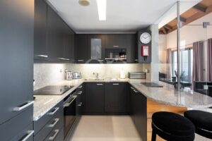 Cuisine moderne gris foncé avec des plans de travail en granit, des appareils électroménagers encastrés et un îlot incurvé équipé de deux tabourets de bar noirs.