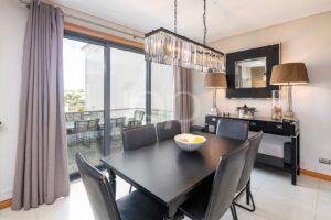 Salle à manger moderne avec une table noire et six chaises en cuir, un lustre en cristal et une console adossée au mur.