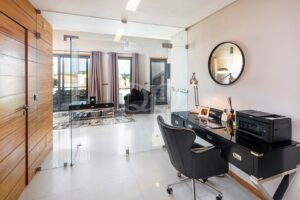 Un bureau à domicile moderne avec une cloison en verre, un bureau noir et une imprimante, aménagé dans un espace de vie lumineux.