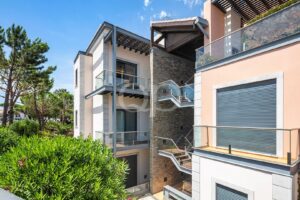 Immeuble moderne à plusieurs étages, doté de balcons vitrés et d'un mur en pierre, niché au cœur d'une végétation luxuriante.