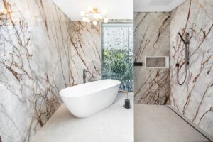 Ein luxuriöses Marmorbad mit einer weißen freistehenden Badewanne, schwarzen Armaturen und einer Trennwand aus Glasmosaik.
