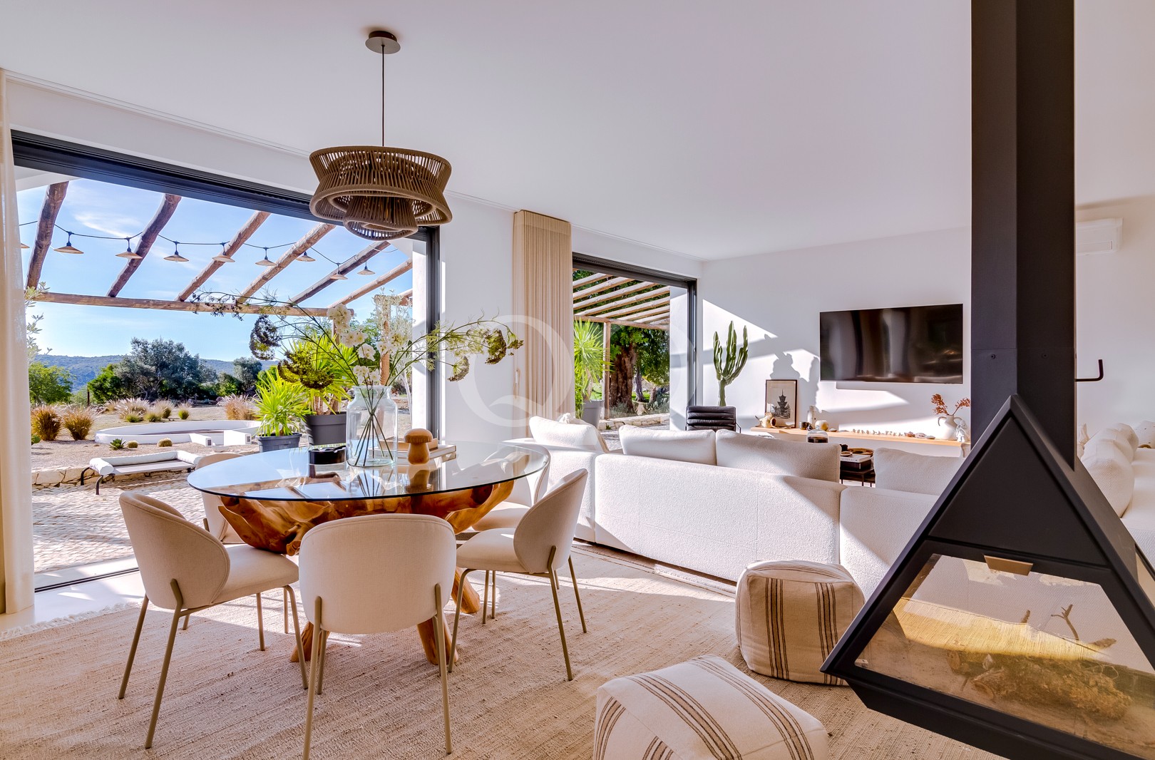 Sala de estar luminosa e moderna, com uma mesa de jantar redonda de vidro, cadeiras em tom creme e grandes janelas com vista para um pátio exterior e para a paisagem do deserto.