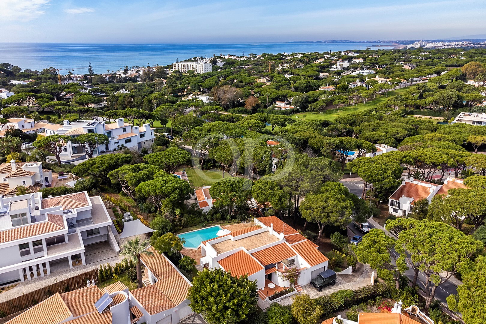 Banlieue côtière avec ses maisons blanches, ses toits de tuiles orange et ses arbres verdoyants et touffus donnant sur la mer.
