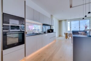 Modern, minimalist kitchen with built-in Siemens appliances, grey cabinets, and under-cabinet lighting along a long counter.