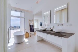 Bright modern bathroom with a freestanding oval tub by a large window, and a double-sink vanity with backlit mirrors.