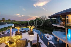 Moderner Poolbereich eines Resorts bei Sonnenuntergang mit Liegestühlen und einem Gebäude mit Glasfassade auf der rechten Seite.
