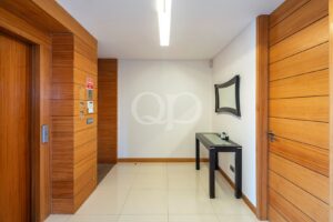Wood-paneled hallway with a glass-topped black console table, curved-framed mirror, and white tiled floor.