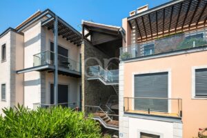 Modern residential building with glass balconies, an external metal staircase, and peach-colored walls under a clear blue sky.
