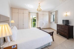 Bright hotel-style bedroom with white bedding, a tall beige headboard, and large built-in wardrobes along the walls.