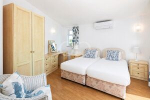 Twin bed setup with matching floral bases, light wood furniture, and blue patterned cushions in a bright, airy bedroom.