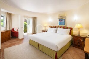 Hotel room with a king-size bed, white linens, and a green-striped headboard; wooden nightstands and lamps on each side.