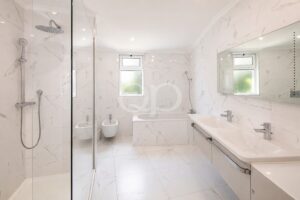 Bright marble bathroom with glass shower enclosure, freestanding tub, and double sink vanity.