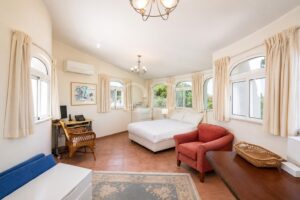 Bright hotel bedroom with a white bed, cream curtains, and multiple arched windows letting in sunlight.