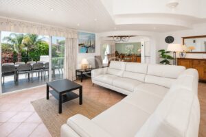 Bright coastal living room with white leather sectional, black coffee table, and sliding glass doors to an outdoor dining area.