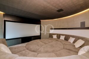 Curved beige sectional seating surrounding a large projection screen in a modern home theater room with ambient lighting.