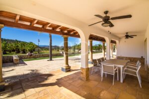 Covered terrace with arched openings, dining area and landscaped garden views