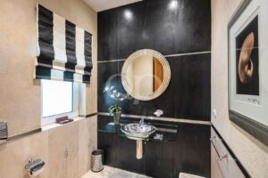 Contemporary bathroom with black tiled wall, round metallic mirror, glass vessel sink, and orchid plant.