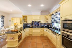 Cream kitchen with an island, navy-blue tiled backsplash, and built-in ovens; blue patterned window shade on the right.
