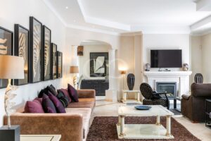 Sala de estar luxuosa com um sofá de veludo castanho, almofadas roxas e uma parede decorada com quadros com motivos de zebra, junto a uma entrada aberta e luminosa.