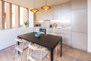 Cozinha moderna e simples, em plano aberto, com iluminação no teto e zona de refeições