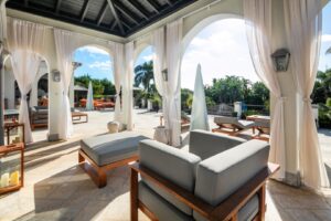 Überdachte Terrasse mit Sitzgelegenheiten und Blick auf den Pool und die Gärten