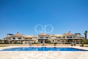 Un luxueux complexe de villas de style méditerranéen, dotées de balcons, entourant une grande piscine extérieure sous un ciel d'un bleu éclatant.