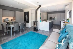 Moderner, offener Küchen- und Wohnbereich mit eleganten Einbaumöbeln, einem Holzofen und lebhaften Akzenten
