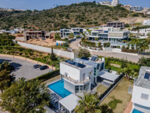 Vista aérea de uma zona residencial numa encosta com casas modernas, um estaleiro de construção na encosta e uma villa branca com uma piscina azul em primeiro plano.