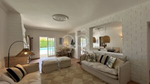 Bright living room with white brick walls, beige sofas, and a view of a pool through glass doors.
