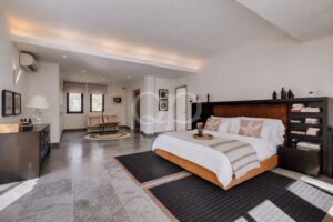 Quarto espaçoso e moderno com uma cama king size, roupa de cama branca, detalhes em bege e uma cabeceira em madeira escura com prateleiras embutidas.