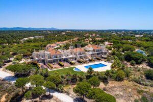 Vue aérienne prise par un drone d'un complexe de villas de luxe aux toits en terre cuite et aux façades beiges, avec une grande piscine bleue trônant au milieu des palmiers et des cours parfaitement entretenues