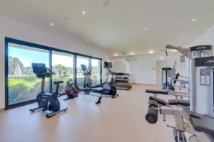 Salle de sport entièrement équipée avec des appareils de cardio, des haltères et des baies vitrées allant du sol au plafond