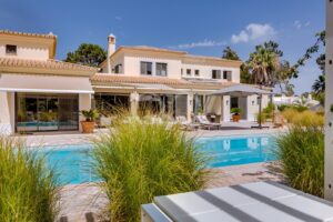 Moradia com fachada mediterrânica em tons de bege, piscina e zona de estar no pátio sob um céu azul límpido