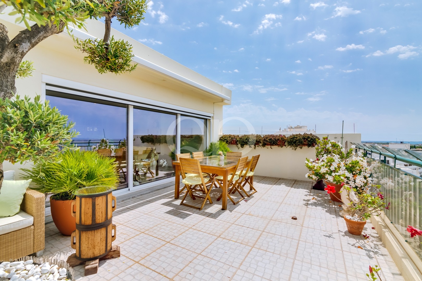 Terraço privado ensolarado, com zona de refeições ao ar livre e vasos com plantas exuberantes