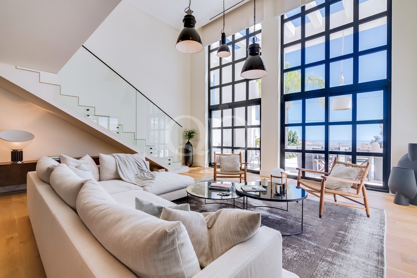 Double height sitting room with floor to ceiling windows and glass staircase