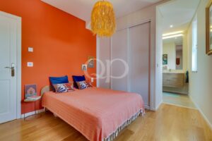 Stylish bedroom with bold orange accents, warm wooden flooring, and a contemporary en-suite