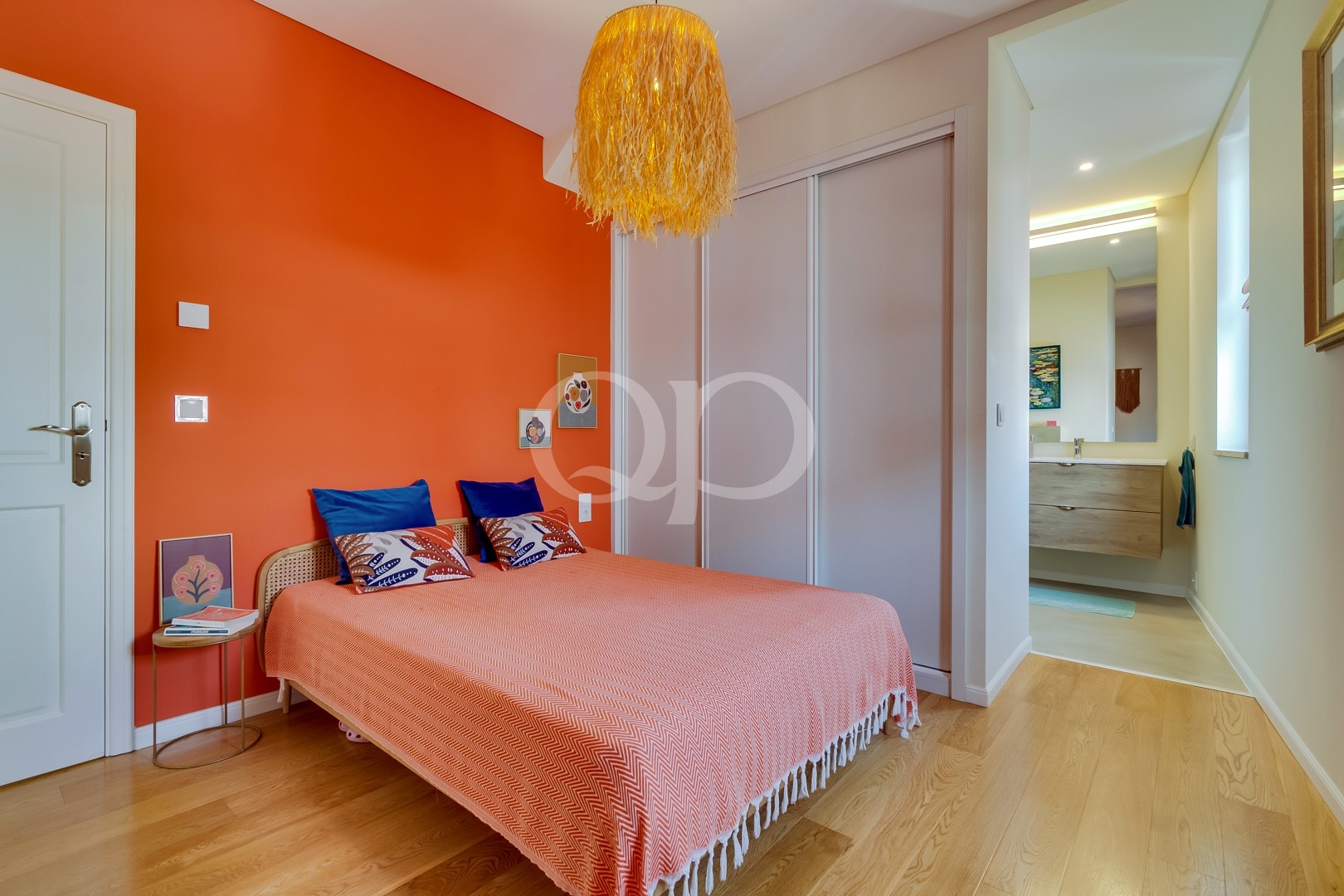 Stylish bedroom with bold orange accents, warm wooden flooring, and a contemporary en-suite