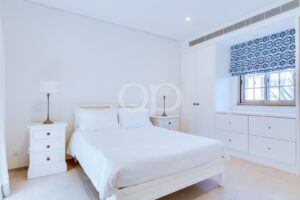Bright white bedroom with a made bed, two white nightstands with lamps, and built-in white drawers.