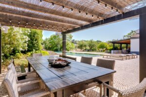 Terraço coberto para refeições ao ar livre, com vista para a piscina e os jardins
