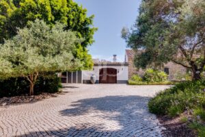 Entrada privada de calçada, rodeada por uma paisagem mediterrânica com árvores maduras