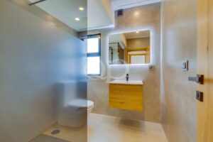Modern bathroom with walk in shower, illuminated mirror and wooden vanity