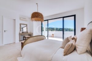 Quarto principal sereno, com texturas naturais, janelas do chão ao teto e vistas pitorescas sobre o campo