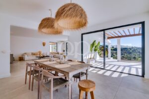 Sofisticada sala de jantar em plano aberto, com candeeiros suspensos em rattan, acesso direto ao terraço e vistas para o campo